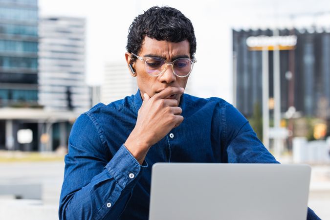 Serious hispanic male freelancer working on laptop in city