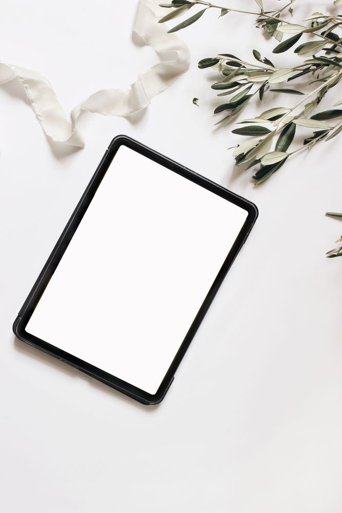 Closeup of tablet with empty screen and olive tree branches and silk ribbon isolated on table