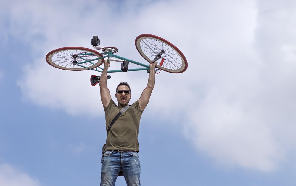 Strong male holding up bike with blue sky and clouds in background