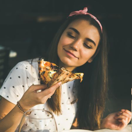 Young woman eating pizza outside in the sun, square crop