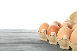 Few raw chicken eggs in carton box on wooden table against light background