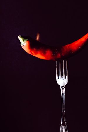 red chili pepper on fire in fork on a dark background
