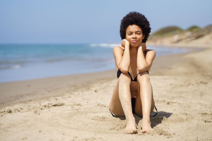 Woman sitting in sand on the beach looking at camera