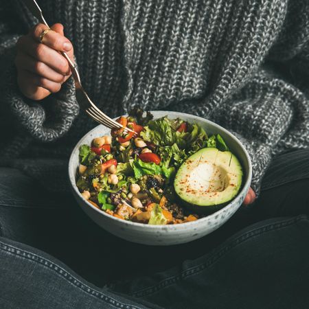 Woman in jeans and sweater eating fresh salad, square crop