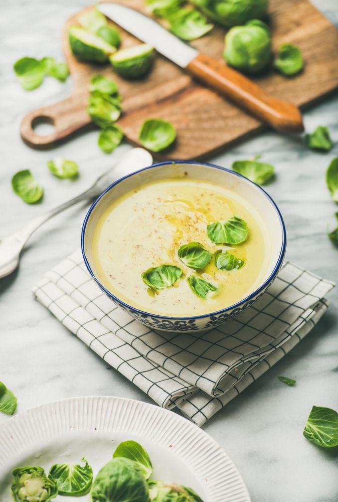 Brussels sprout soup, garnished with fresh sprouts, next to wooden board, vertical composition