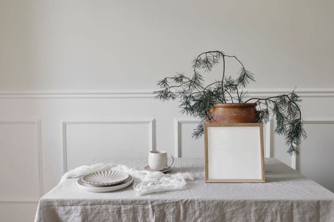 Festive winter dinner table setting with cup of coffee, plates and pine tree branches in large pot with mock up frame