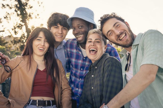 Happy group of diverse young friends smiling and laughing outdoors at sunset.