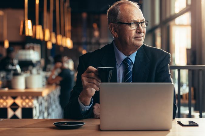 Mature entrepreneur sitting at coffee shop with laptop on table