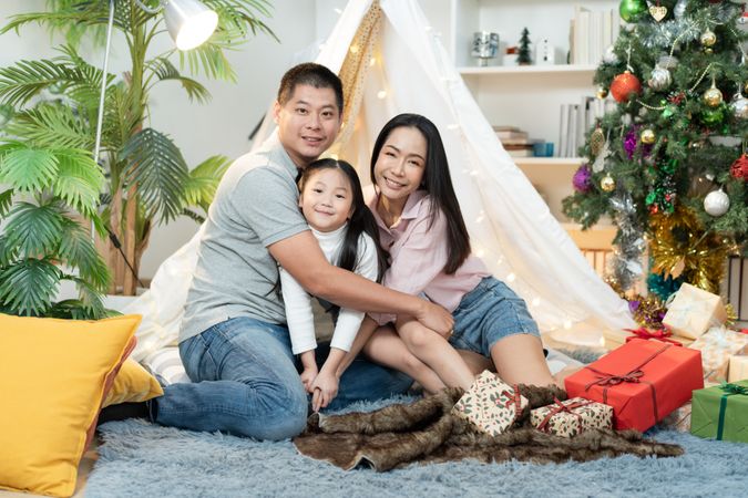 Happy Asian family embracing and sitting at cozy tent looking at camera