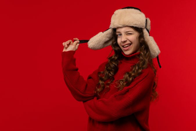 Playful girl in red sweater and fur hat winks