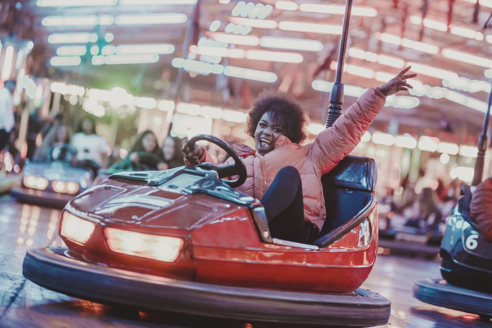 Excited Black woman riding car in amusement park