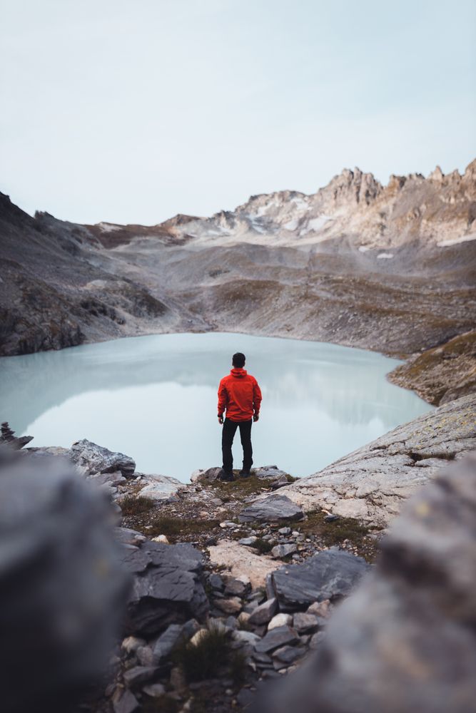 Back view of man in red jacket standing on waterside of frozen lake