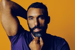 Sensual Black man in yellow studio with one hand to his chin with arm behind his head