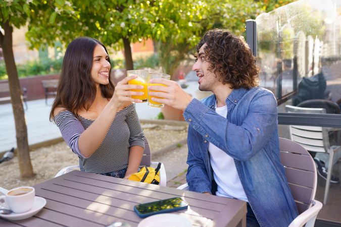 Man and woman smiling at each other with their orange juice outside