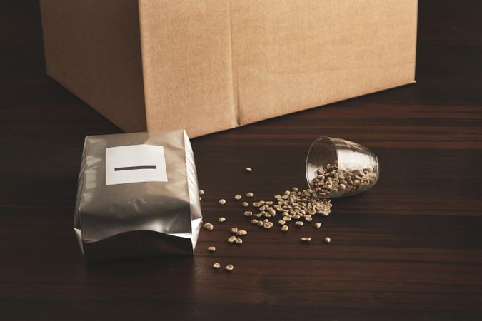 Bag of coffee beans in front of card board box with spilled whole beans
