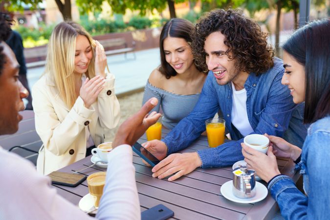 Happy friends looking at phone over coffee and juice on outside table