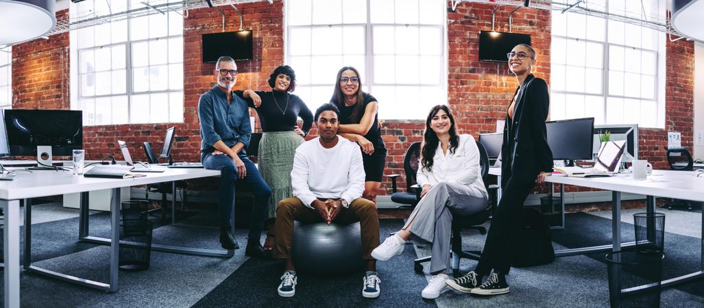 Wide shot of modern businesspeople smiling at the camera in a creative office