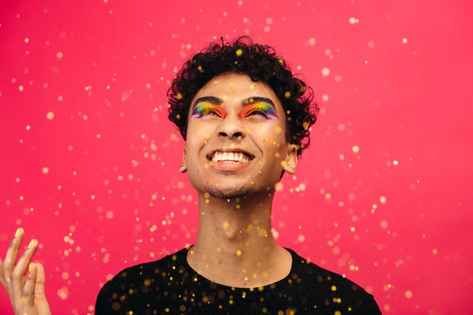 Cheerful man with rainbow eye makeup throwing up the glitter