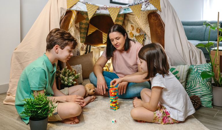 Happy family having fun playing together with wooden stacking piece game in front of homemade tent