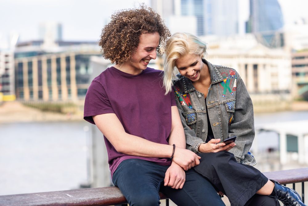 Laughing couple sitting with each other while on fence over river