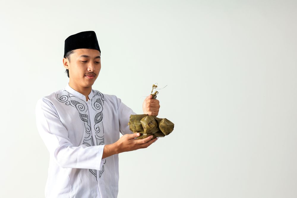Muslim Asian Man Wearing Shirt Baju Koko  and Black Caps Kopyah Holding ketupat Rice Cakes