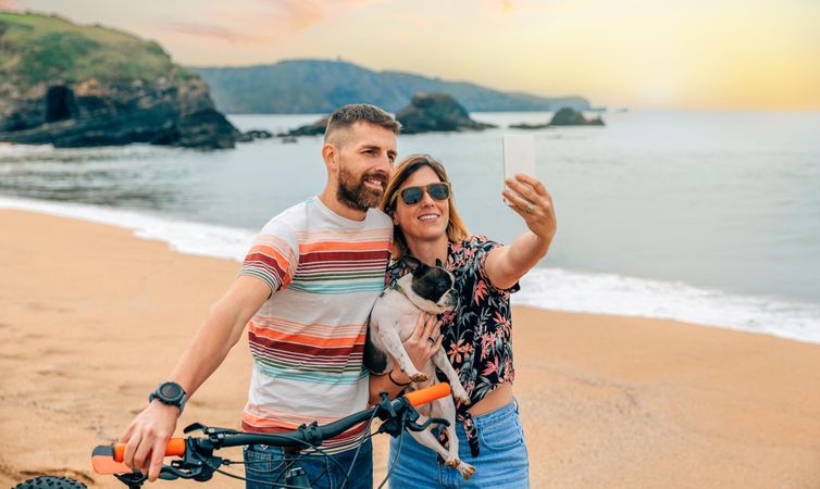 Male and female taking picture of themselves with their pet dog along the coast