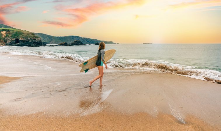 Woman standing on the shore with surfboard walking into the ocean
