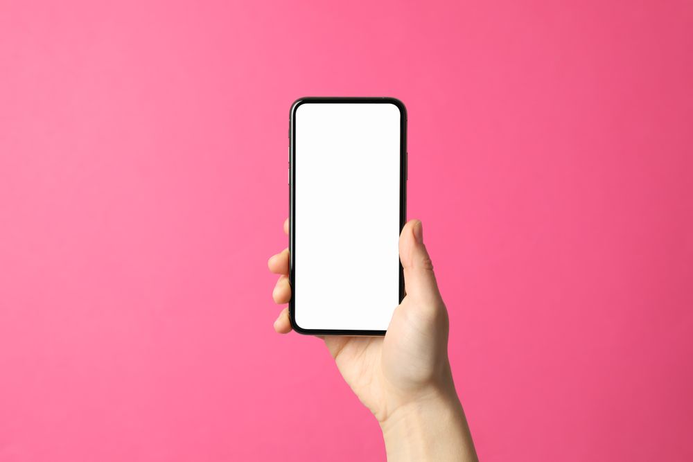Female hand holds phone on pink background. Empty screen