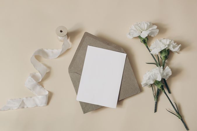 Carnation flowers, eucalyptus branches and ribbon on beige table with blank card