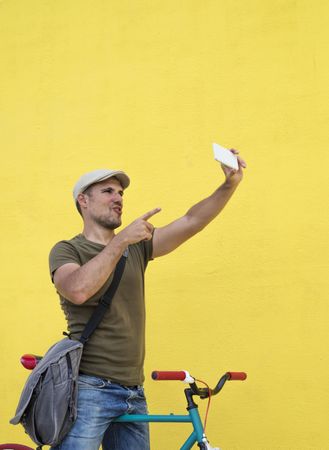 Male in hat and sunglasses taking selfie on phone while sitting on bicycle, vertical