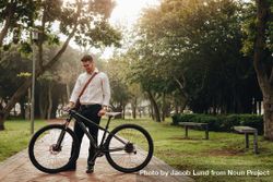 Smiling businessman looking at his bike standing in the park 4AMlQ4