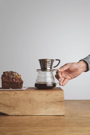 Man reaching for pour over coffee next to slide of cake