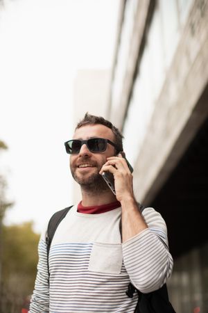 A young, traveling man wearing sunglasses, talking on a smartphone phone, on the street, in a city in Spain