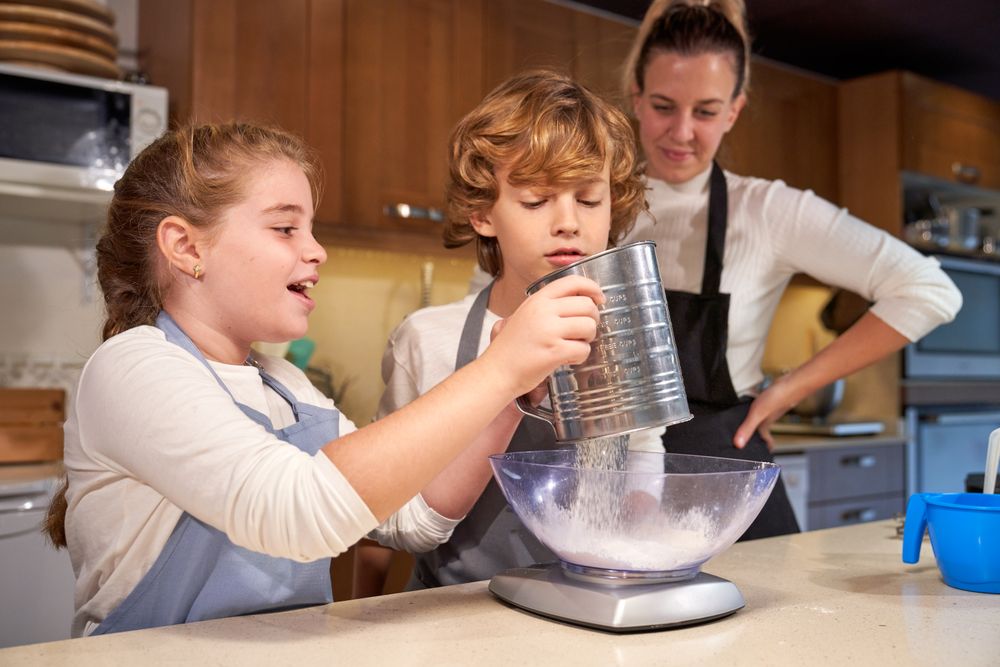 Cheerful girl sifting flour into bowl during cooking process