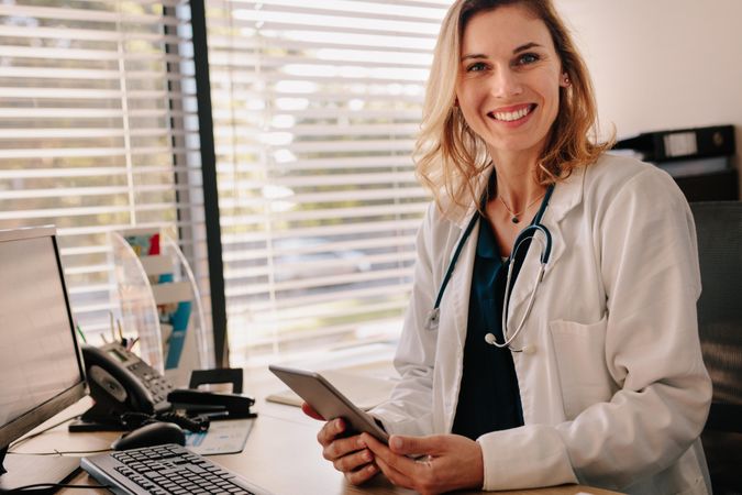Female doctor sitting at her desk holding a digital tablet