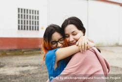 Two young women hug each other outside with eyes closed 4ZeeyA