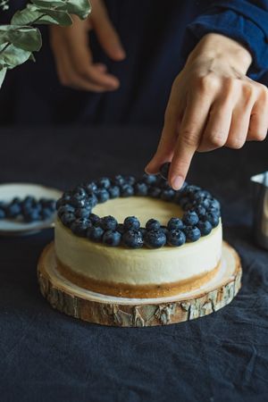Person decorating cheesecake dessert with fruit
