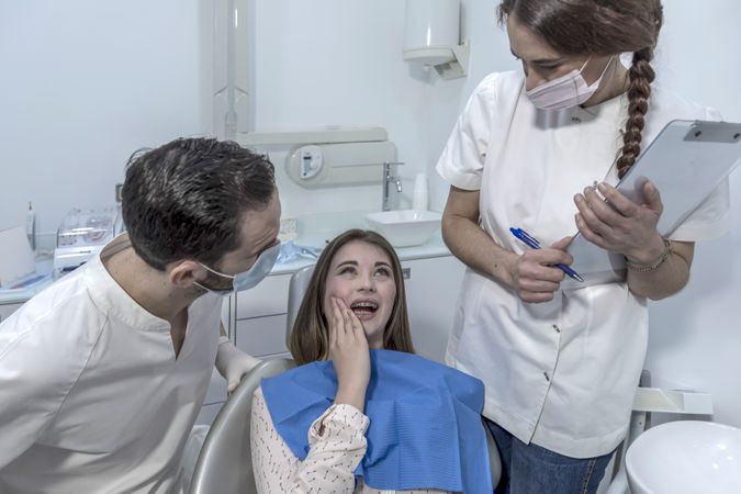 Teenage girl with tooth pain sitting to dental chair