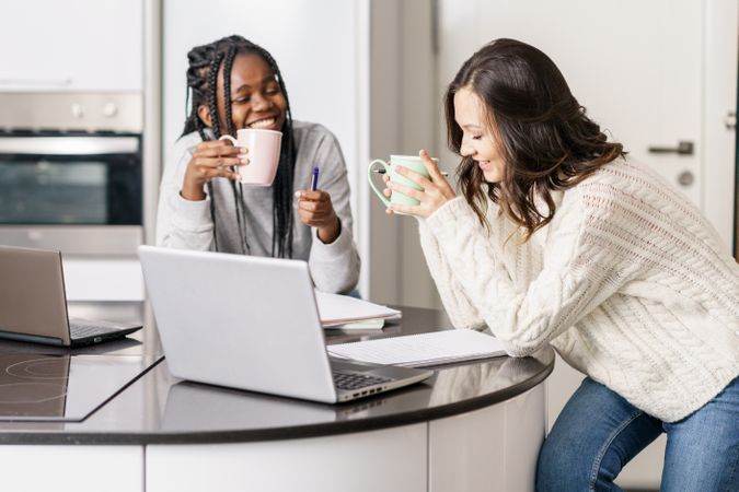 Two women laughing together at the kitchen table with a laptop