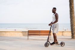 Cool adult Black man riding scooter in street