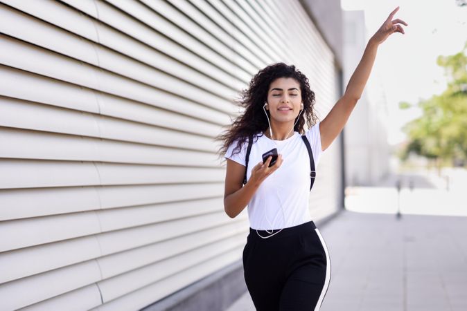 Arab woman in sport clothes with curly hair walking outside while dancing and pointing up