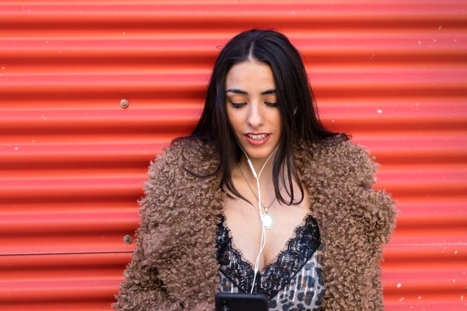 Trendy woman with smartphone near wall