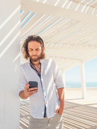 Relaxed man using smartphone in gazebo on beach