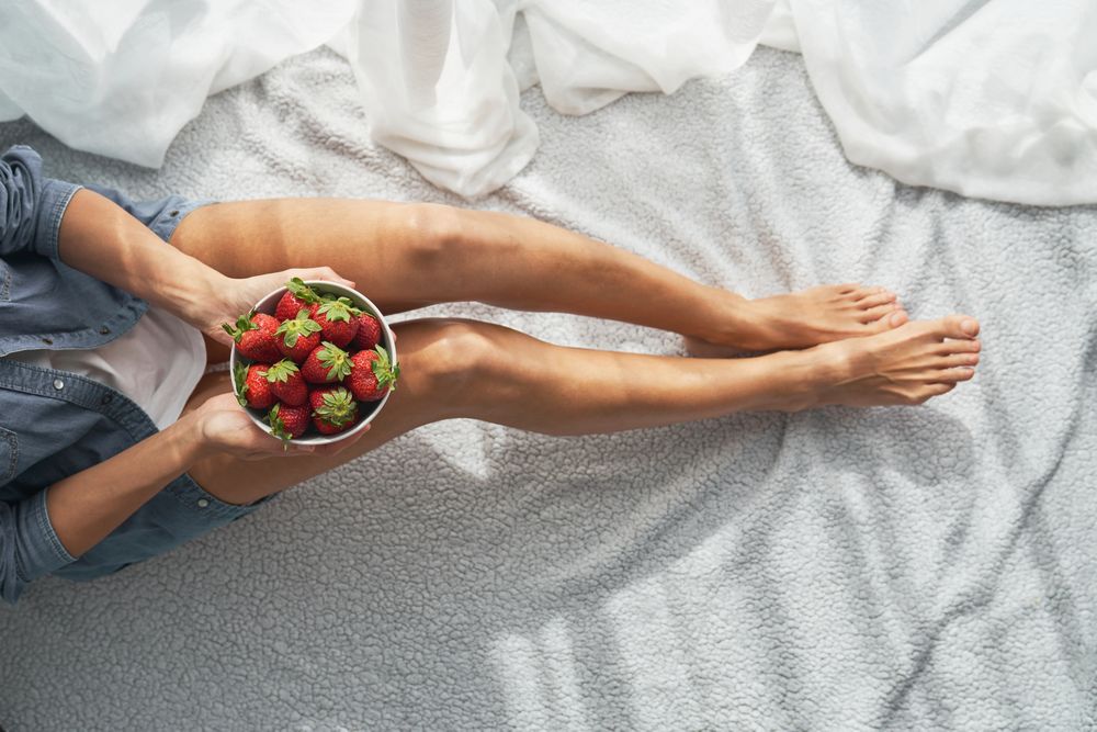 Faceless person with bowl of fresh strawberries on fabric