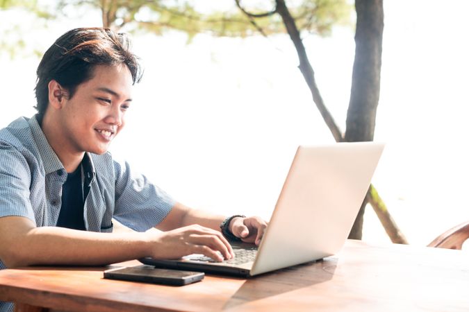 Happy Asian Young businessman work at outdoor with laptop. Concept of remote and freelance work. Young successful man wearing casual blue cloth.