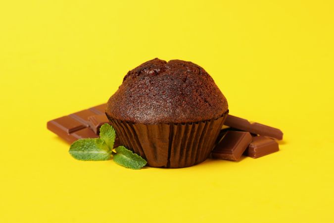 Tasty muffin and chocolate on yellow background