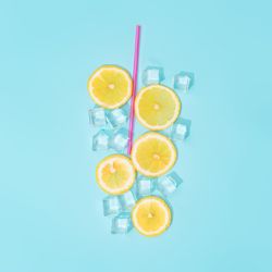 Creative summer background composition with lemon slices, straw and ice cubes