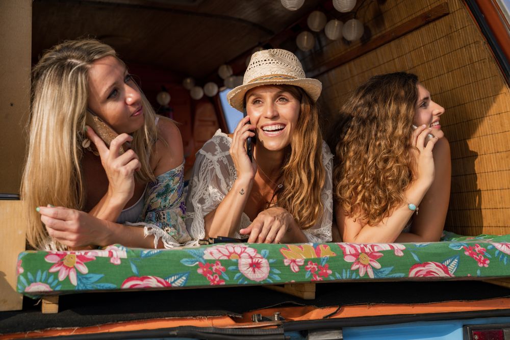 Content female friends browsing smartphone placing on open trunk of car