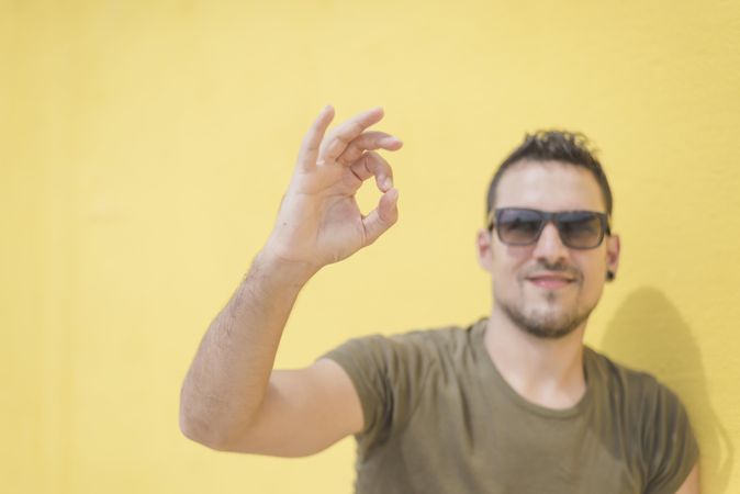 Male making “a-ok” sign in front of yellow wall outside