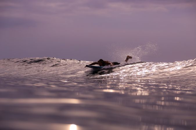 Man on surf board on waving water at sunset